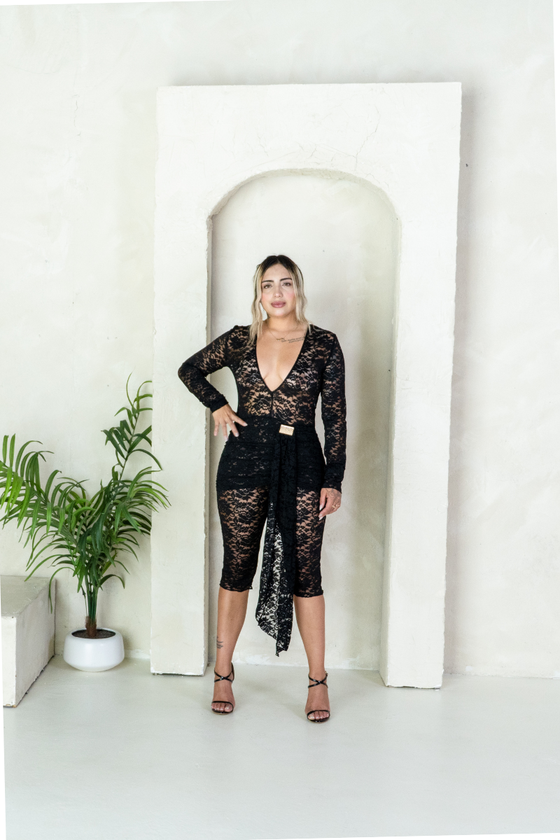 Woman in a black lace outfit standing in a white room with a plant.